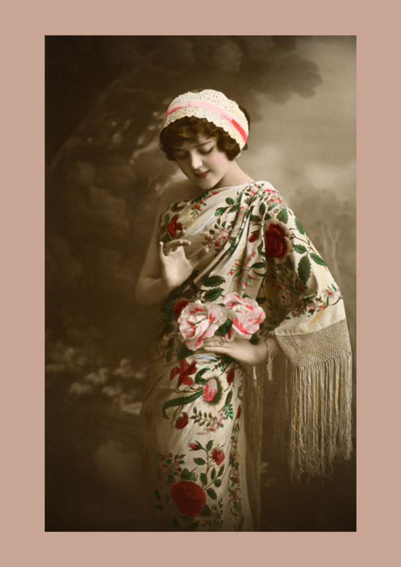 Portrait en pied d'une jeune femme vêtue d'une robe aux riches motifs floraux, portant un châle à longues franges. Cette carte postale photographique témoigne de l'évolution de la mode féminine au début du XXᵉ siècle.