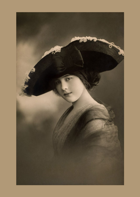 Portrait d'une jeune femme coiffée d'une large capeline ornée d'un délicat galon. Cette carte postale photographique de la Belle Époque met en valeur l'élégance des grands chapeaux féminins du début du XXᵉ siècle.