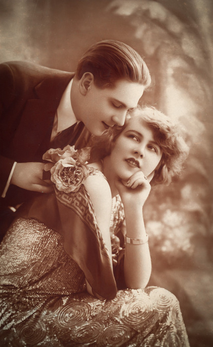 Anne et Léon – Une promesse murmurée Dans cette carte postale ancienne des années 1920, Léon se rapproche d'Anne avec tendresse. Le bouquet de roses qu'il lui offre souligne cette scène pleine de romantisme.