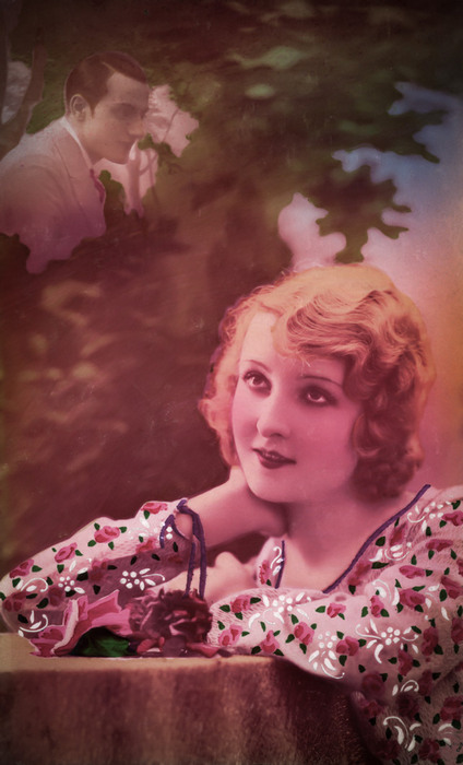 Augusta et le baiser rêvé – Photomontage romantique vers 1925 Dans cette carte postale des années 1920, Augusta rêve d’un baiser, tandis que la silhouette de son amoureux apparaît en arrière-plan. Le jeu de superposition et de transparence crée une apparition délicate, caractéristique des photomontages romantiques de l’époque.