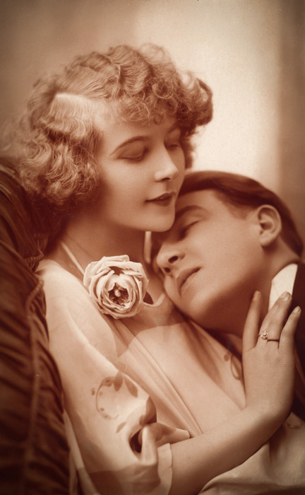 Marguerite et Abel – Le repos des cœurs Dans ce portrait sentimental des Années folles, Marguerite accueille tendrement Abel contre elle. Une rose souligne la douceur de cette carte postale ancienne.