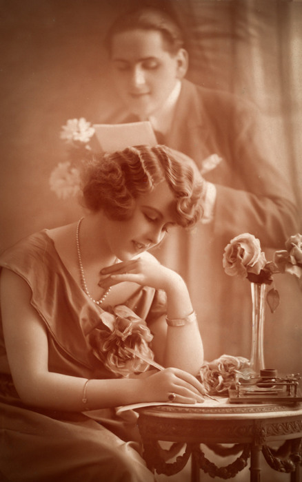 La Lettre d'Anne – Photomontage romantique vers 1920 Dans cette carte postale des années 1920, Anne écrit une lettre à son amoureux, tandis que son image apparaît en arrière-plan. Le subtil jeu de superposition et de transparence révèle toute la virtuosité du photomontage à cette époque.