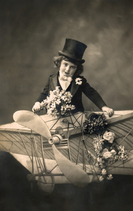 Arthur – Premier rêve d'aviation Arthur prend place à bord d’un aéroplane reconstitué en studio et décoré de fleurs. Cette carte postale photographique témoigne de la fascination naissante pour l’aviation et des rêves de voyage qui accompagnent les débuts de l’aéronautique.
