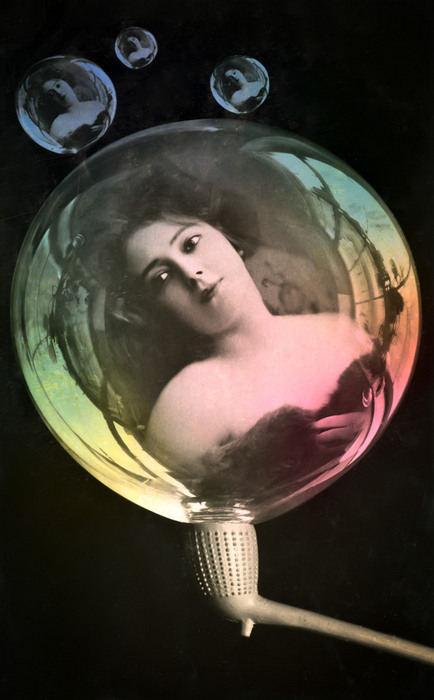 La bulle de savon – Portrait féminin vers 1900 Dans cette carte postale de la Belle Époque, une jeune femme apparaît au cœur d’une grande bulle de savon, tandis que trois bulles plus petites renferment d’autres portraits. Les effets de transparence et les reflets colorés donnent à cette composition une dimension particulièrement surprenante.