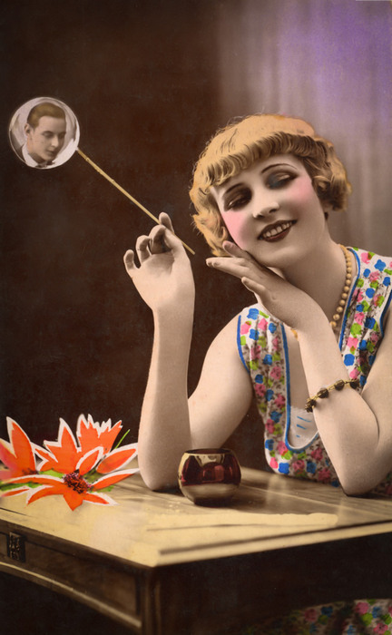La bulle de savon – La souffleuse de bulles vers 1900 Dans cette carte postale de la Belle Époque, une jeune femme semble souffler une bulle de savon contenant le portrait photographique d’un homme. Ce jeu d’illusion transforme la bulle en un étonnant écrin pour le portrait et témoigne de l’inventivité des compositions photographiques de l’époque.