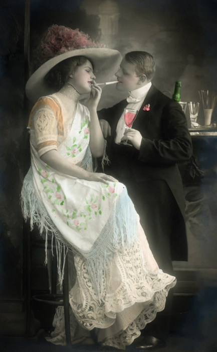 Élise et Auguste – Conversation élégante Élise est vêtue d'une robe claire à franges et est coiffée d'un large chapeau. Elle échange un regard complice avec Auguste en costume sombre. Cette carte postale photographique illustre l'élégance des couples de la Belle Époque.