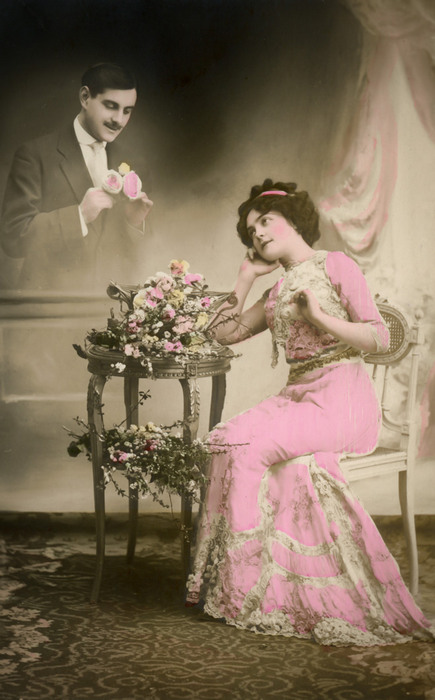 Emma et la rose d'amour – Photomontage romantique vers 1900 Dans cette carte postale de la Belle Époque, une jeune femme contemple le bouquet de roses que lui a offert son amoureux. Le photomontage fait surgir derrière elle la silhouette de celui qu’elle aime.