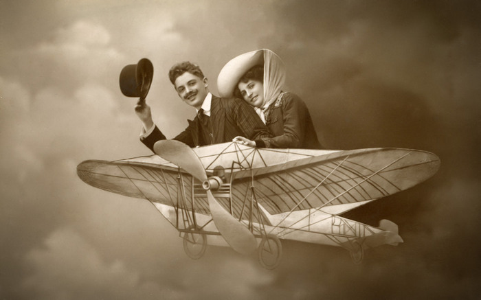 Ernestine et Clotaire – En route vers les nuages Ernestine et Clotaire prennent place dans un aéroplane, en route vers les nuages, tandis que Clotaire lève son chapeau. Cette carte postale photographique de la Belle Époque nous entraîne dans l’imaginaire des premiers rêves d’aviation.