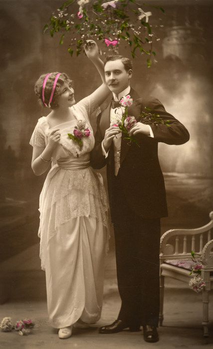 Julia et Harold – Sous les fleurs Julia et Harold se tiennent côte à côte sous une branche de fleurs. Julia porte une robe claire drapé tandis qu'Harold arbore un élégant costume sombre.