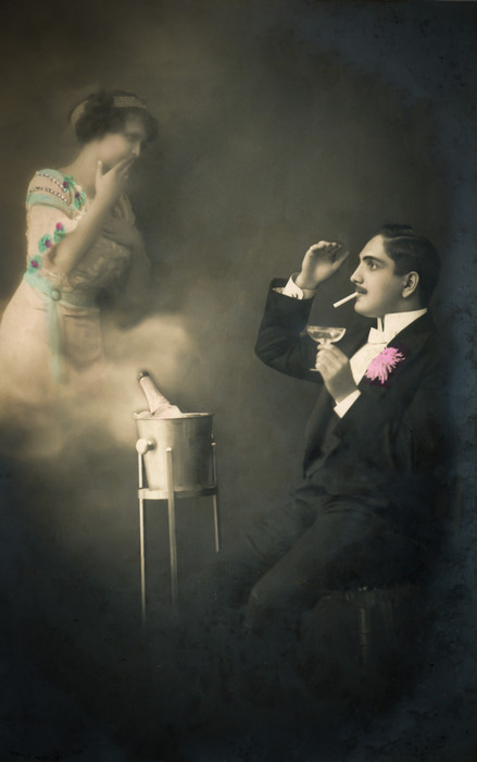 L’apparition de Lucien – Photomontage romantique vers 1900 Dans cette carte postale de la Belle Époque, Lucien fume une cigarette tandis qu’une femme apparaît dans un nuage de fumée. Le photomontage et les effets de transparence créent une étonnante apparition, témoignant de la virtuosité technique des créateurs de l’époque.