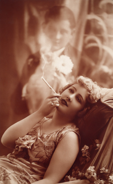 Marie-Louise rêvant – Photomontage romantique vers 1900 Dans cette carte postale de la Belle Époque, une jeune femme songe à son amoureux en fumant une cigarette. Son image apparaît dans un halo de fumée, un effet de photomontage qui témoigne de l’étonnante virtuosité technique des créateurs de l’époque.