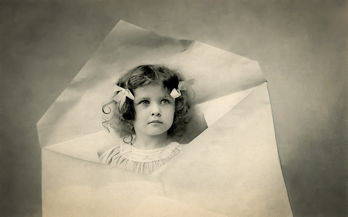L'enveloppe – Portrait d'enfant vers 1900 Dans cette carte postale de la Belle Époque, une fillette apparaît au cœur d’une enveloppe ouverte. Le jeu de découpe et de relief donne l’illusion que son portrait surgit directement du papier.