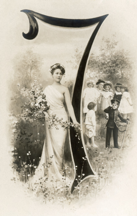 Chiffre illustré 7 – Belle Époque Dans cette carte postale de la Belle Époque, une jeune femme et sept enfants prennent place autour du chiffre 7, au cœur d’un paysage arboré. Le bouquet de fleurs et la végétation s’intègrent naturellement à la composition.