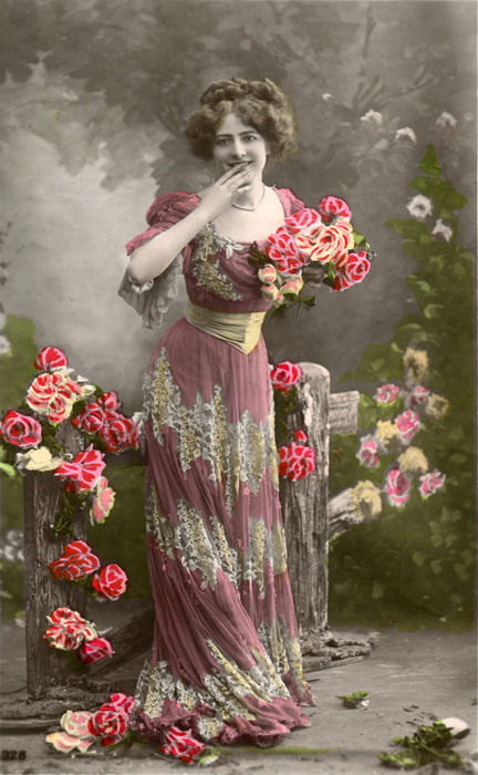 Lucienne parmi les roses | Décor peint Lucienne tient un bouquet de roses devant un décor peint représentant un jardin. La colorisation, réalisée dans les ateliers spécialisés de l’époque, rehausse les fleurs et les détails de son costume.