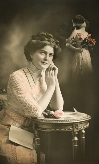 Léone rêvant – Photomontage romantique vers 1900 Dans cette carte postale de la Belle Époque, Léone, songeuse, imagine une scène d’amour. Le photomontage fait apparaître derrière elle l’image d’un couple dans une atmosphère délicatement romantique.