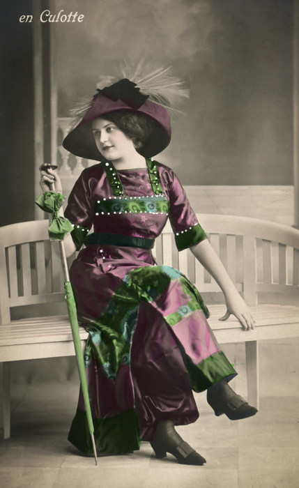 Renée – Élégance en jupe-culotte Renée est vêtue d'une élégante jupe-culotte et coiffée d'un large chapeau orné d'une plume. Ce portrait photographique témoigne des innovations de la mode féminine au début du XXᵉ siècle.